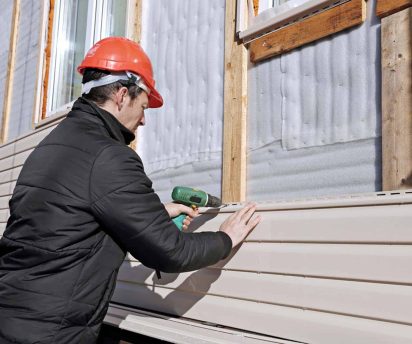 A worker installs panels beige siding on the facade of the house