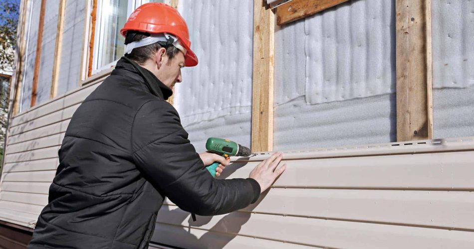 A worker installs panels beige siding on the facade of the house
