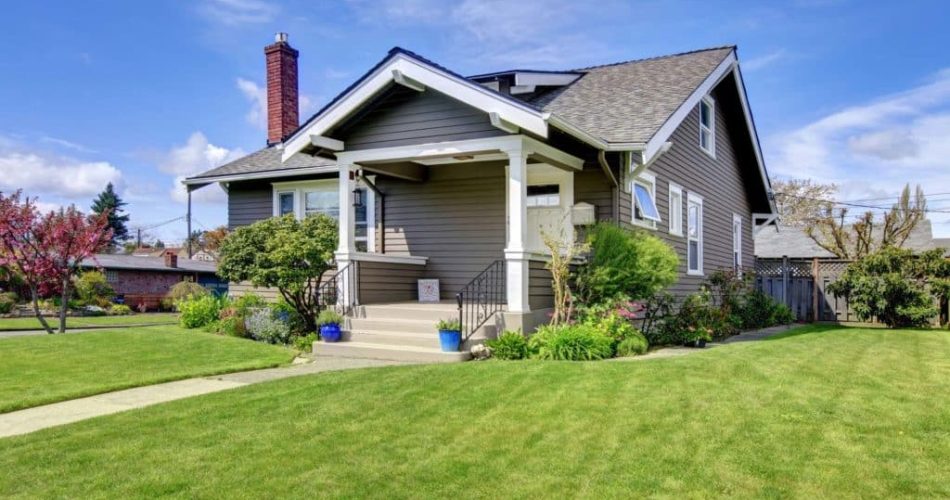Clapboard siding house with tile roof and brick chimney. View of white column porch and green lawn