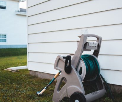 Garden hose coiled next to home siding wall during seasonal exterior maintenance check